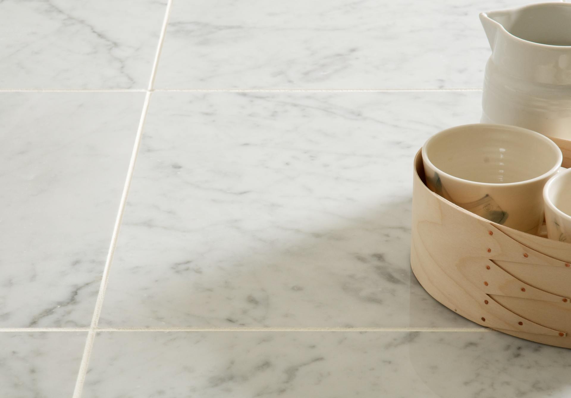 Pale marble tiles with fine grey veining beside ceramic tableware