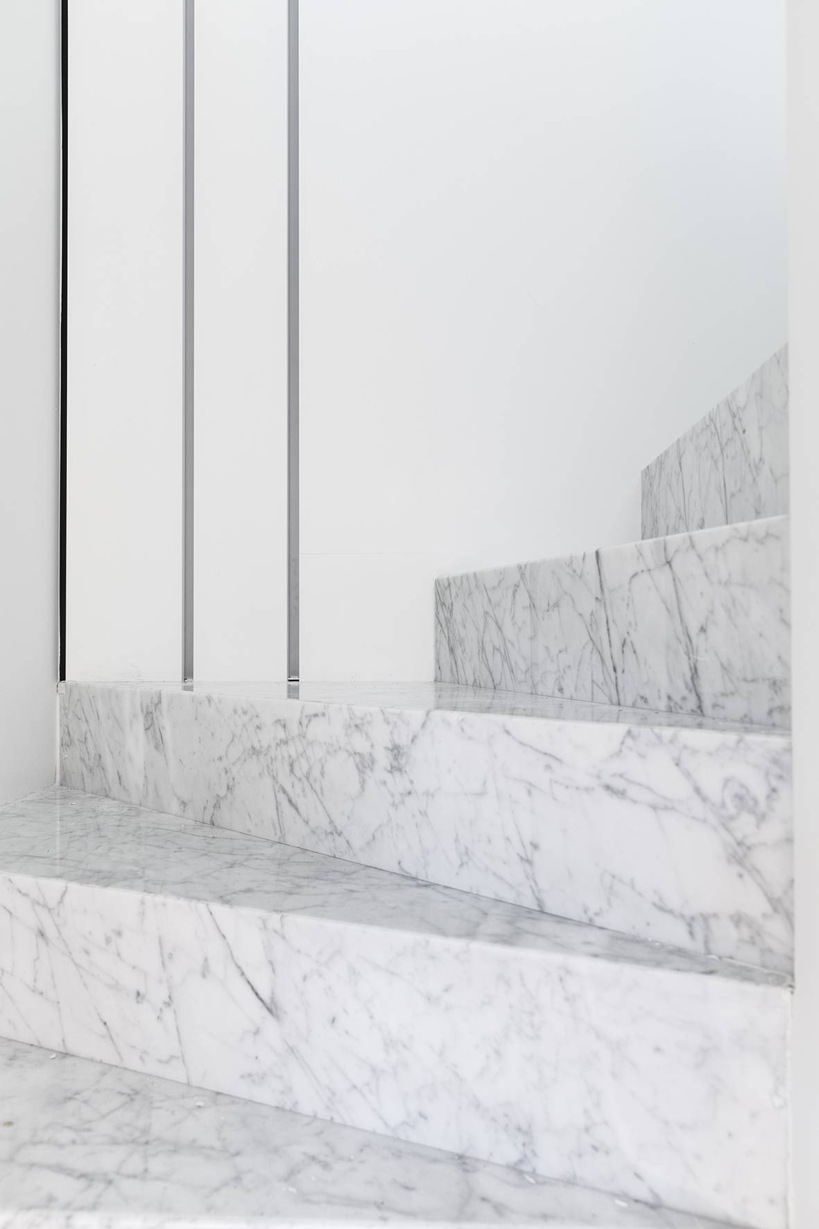 White marble staircase with grey veining and a slim metal balustrade